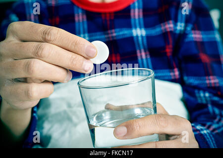 Primo piano di un giovane uomo caucasico in pigiama nel letto circa a mettere una compressa effervescente in un bicchiere con acqua Foto Stock