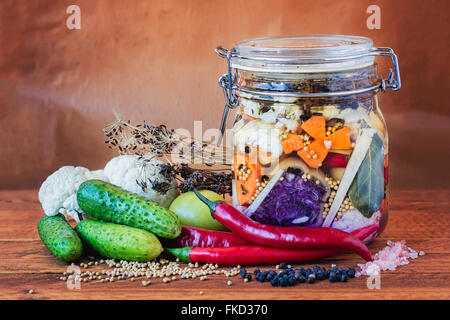 Jar assortiti di messi in salamoia lacto-fermentati sottaceti su un tavolo di legno circondato da spezie e verdure. Foto Stock