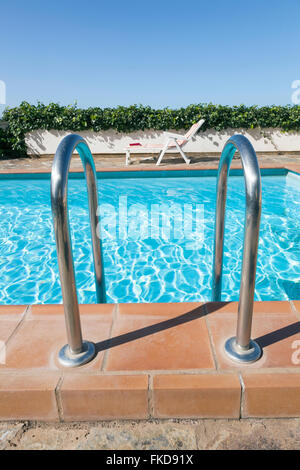 Ingresso alla piscina con edera sul muro e cielo blu e sedia a sdraio in background Foto Stock