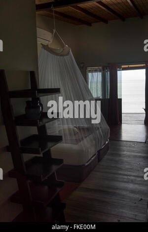 Gli interni di località turistica camera da letto e vista sul mare attraverso la porta aperta, Trinidad, Trinidad e Tobago Foto Stock