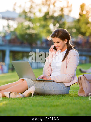 Imprenditrice nel Parco lavorando su laptop, rendendo chiamata telefonica Foto Stock