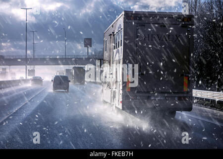 Automobili e camion guida su autostrada durante il nevischio causando pericolosi bagnato invernale le condizioni delle strade in inverno / molla Foto Stock