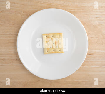 Vista dall'alto di un insipido saltine cracker su una piastra bianca in cima a una tavola di legno alto. Foto Stock