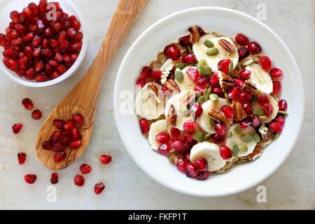 Sana colazione fiocchi d'avena con melograno, banane, semi e noci, overhead di scena sul marmo bianco Foto Stock