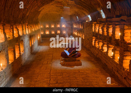 Un giovane monaco di lettura con raggi di sole e in templi di Bagan, Myanmar Foto Stock