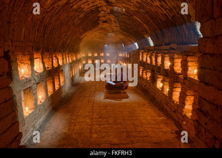 Un giovane monaco di lettura con raggi di sole e in templi di Bagan, Myanmar Foto Stock