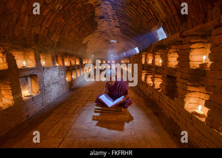 Un giovane monaco di lettura con raggi di sole e in templi di Bagan, Myanmar Foto Stock