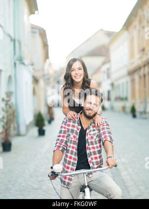 Felice coppia giovane di andare per un giro in bicicletta in città su una soleggiata giornata estiva Foto Stock