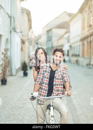 Felice coppia giovane di andare per un giro in bicicletta in città su una soleggiata giornata estiva Foto Stock