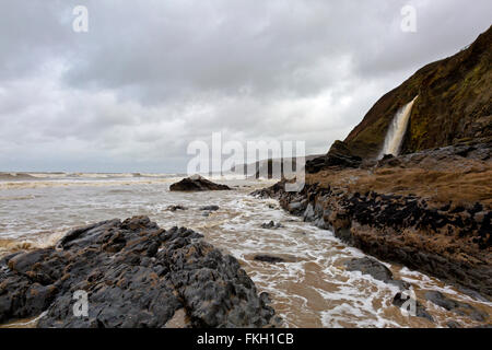 Un selvaggio, piovoso, coudy, tempestoso giorno sulla costa gallese in Pembrokeshire con cascata, scogliere, rocce e surf Foto Stock