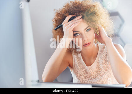Ritratto di pensosa bella donna giovane designer azienda matita e con tavoletta grafica Foto Stock