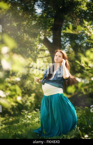 Bella donna incinta in vestito blu per godersi la natura e sole in estate verde parco. A piena altezza verticale, cercando nella fotocamera. Foto Stock