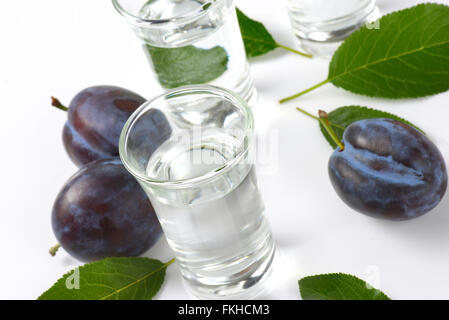 Slivovitz (brandy alla prugna) e prugne fresche su sfondo bianco Foto Stock