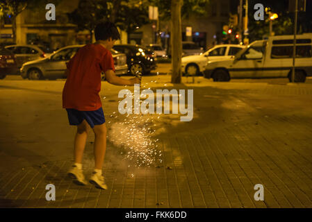 Ragazzo esplodere petardi durante la notte per celebrare la festa di sant Joan su una strada di Barcellona e della Catalogna, Spagna Foto Stock