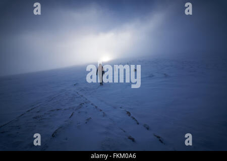 Un escursionista e il loro cane avvicinarsi al vertice di Cairn Gorm come il sole combatte attraverso il cloud, Highlands scozzesi, UK. Foto Stock
