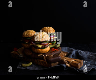 Fresca hamburger di manzo con formaggio, verdure, sottaceti e piccante salsa di pomodoro su carta su rustiche tavole in legno sfondo nero, s Foto Stock