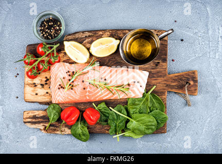 Ingredienti per la cottura sana la cena. Materie filetto di salmone, spinaci, pomodori, olio d'oliva, limone, peperoncino, rosmarino e spezie su Foto Stock