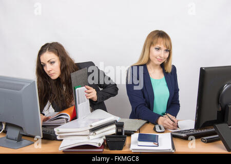 I colleghi in ufficio ragazze, sia guardando al primo monitor con un mucchio di documenti e cartelle, seconda solo al foglio o Foto Stock