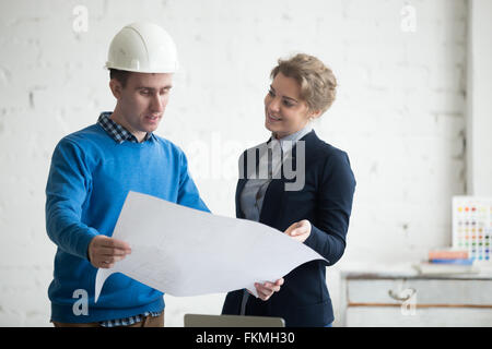 Due giovani colleghi alla riunione guardando al concetto di progetto, tenendo blueprint, lavori di pianificazione. Discussione aziendale Foto Stock