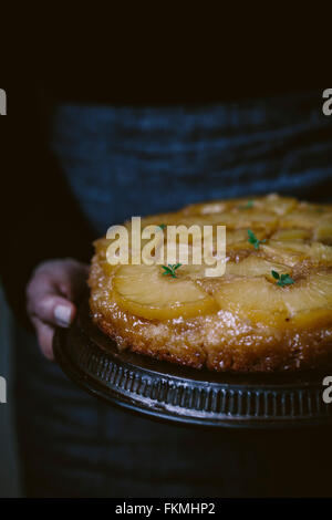 Una donna è stata fotografata dalla parte anteriore mentre si tiene un ananas Torta capovolta. Foto Stock