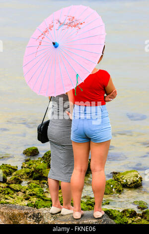 Due ragazze in piedi al bordo delle acque di Tampa Bay tenendo un ombrellino di carta Foto Stock