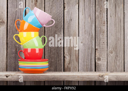 Colorate tazze di caffè sul ripiano contro la rustica parete in legno con spazio di copia Foto Stock