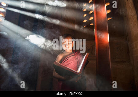 Un giovane monaco di lettura con raggi di sole e in templi di Bagan, Myanmar Foto Stock