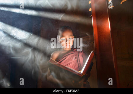 Un giovane monaco di lettura con raggi di sole e in templi di Bagan, Myanmar Foto Stock