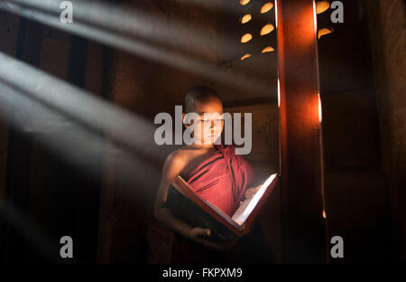 Un giovane monaco di lettura con raggi di sole e in templi di Bagan, Myanmar Foto Stock