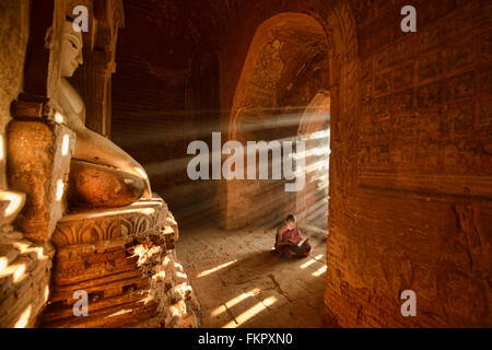 Un giovane monaco di lettura con raggi di sole e in templi di Bagan, Myanmar Foto Stock