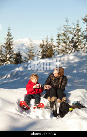 Caucasian madre e figlio di bere cioccolata calda nella neve Foto Stock