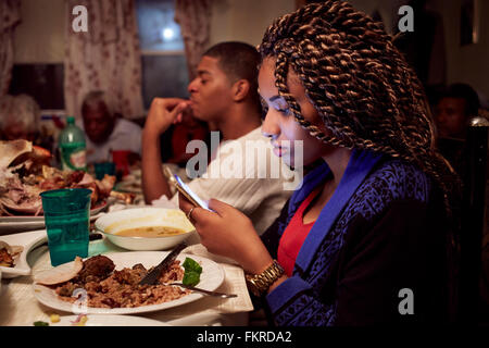 Ragazza adolescente tramite telefono cellulare al tavolo per la cena Foto Stock