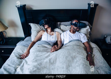 Coppia utilizzando la realtà virtuale occhiali a letto Foto Stock