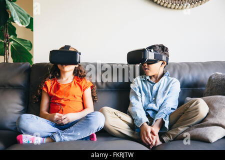 Razza mista bambini utilizzando la realtà virtuale gli occhiali sul divano Foto Stock