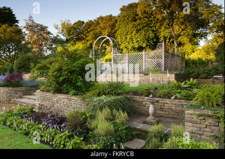 I terrazzamenti con bordo erbacee, piante, trellis arch & Bird - Bagno bello, progettato, giardino paesaggistico, Burley in Wharfedale, nello Yorkshire, Inghilterra. Foto Stock