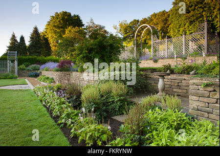 I terrazzamenti con prato, Herbaceous borders, piante e traliccio arch - bella, progettato e paesaggistici, giardino, Burley in Wharfedale, nello Yorkshire, Inghilterra. Foto Stock