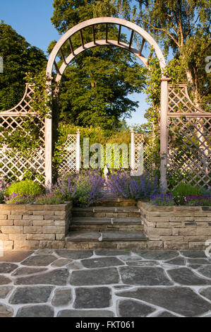 Vista della scultura attraverso il soleggiato trellis arbour archway - disegnate splendidamente paesaggistici, tradizionale giardino, Burley in Wharfedale,Yorkshire, Inghilterra. Foto Stock