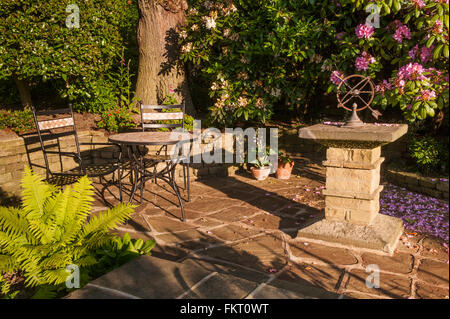 Tavolo e sedie e meridiana di pietra, sul patio in estate il sole - bella e tradizionale, giardino paesaggistico, Burley in Wharfedale, nello Yorkshire, Inghilterra. Foto Stock