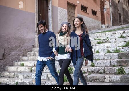 Gli amici passeggiando per le scale in pietra a braccetto sorridente Foto Stock