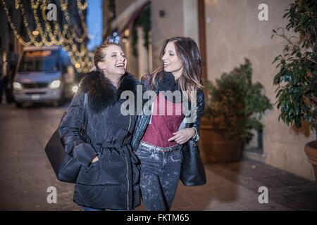 Giovani donne camminando per strada la sera a braccetto di ridere Foto Stock