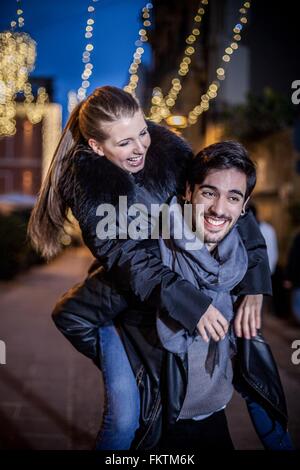 Giovane uomo dando giovane donna piggyback sorridente Foto Stock