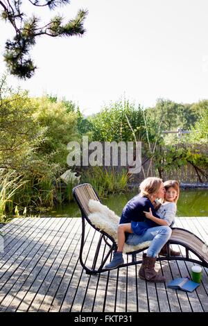 Madre e figlia costeggiata sulla sedia a sdraio in decking Foto Stock