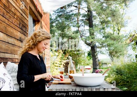 Giovane donna tritare verdure a tavola all'aperto Foto Stock