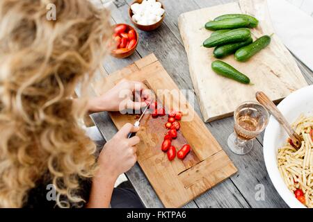 Donna Tritare i pomodori sul tagliere di legno, alto angolo Foto Stock