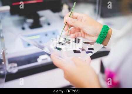 Donna scienziato utilizzando uno spettrofotometro FTIR, tenendo la pellicola sottile di campione per la misurazione Foto Stock