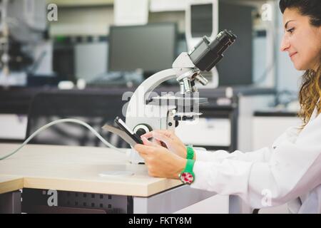 Donna scienziato utilizzando tavoletta digitale e microscopio ottico Foto Stock