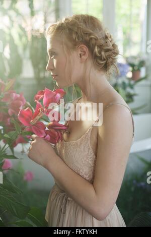 Ritratto di giovane donna bionda capelli intrecciati, profumati fiori di colore rosa Foto Stock