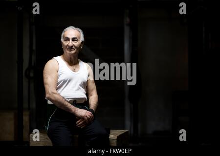 Ritratto di capelli grigi senior uomo seduto nel buio della palestra Foto Stock