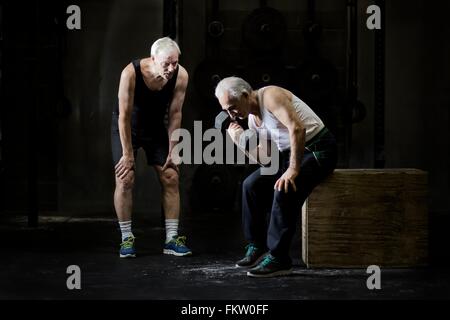 Alti uomini della formazione con il manubrio nella palestra scuro Foto Stock