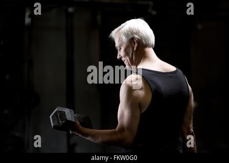Senior uomo facendo bicipite ricci con il manubrio in palestra scuro Foto Stock